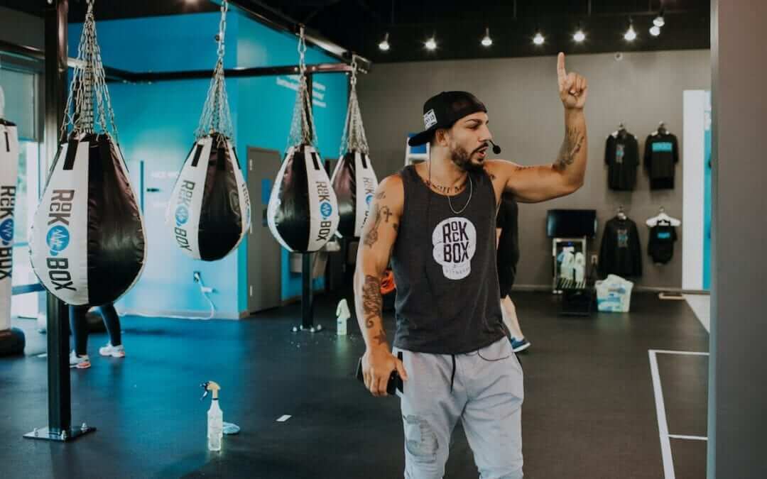 Coach standing in rockbox gym speaks on a microphone while holding up one finger