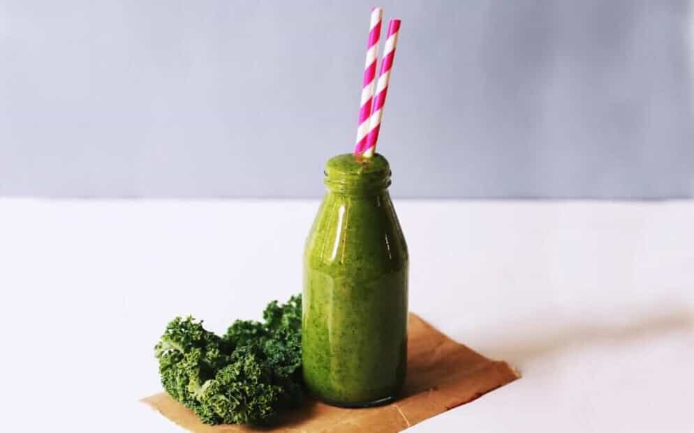 A green smoothie with kale next to it and straws in the bottle
