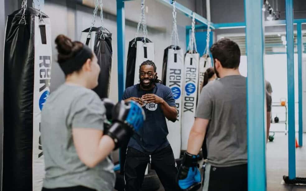 Three people speaking in a gym wearing boxing gloves