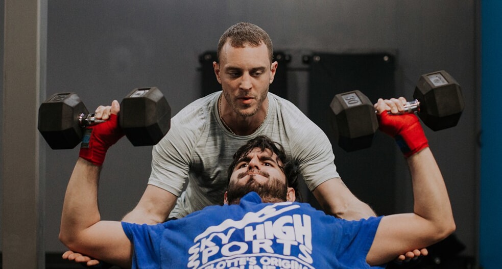a rockbox employee spots a member lifting weights